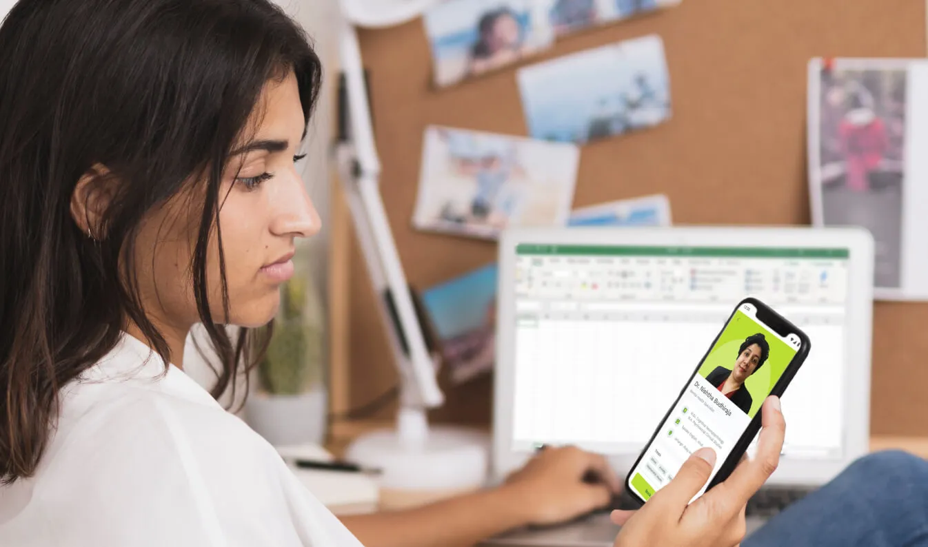 a woman sitting in front of a computer holding a cell phone